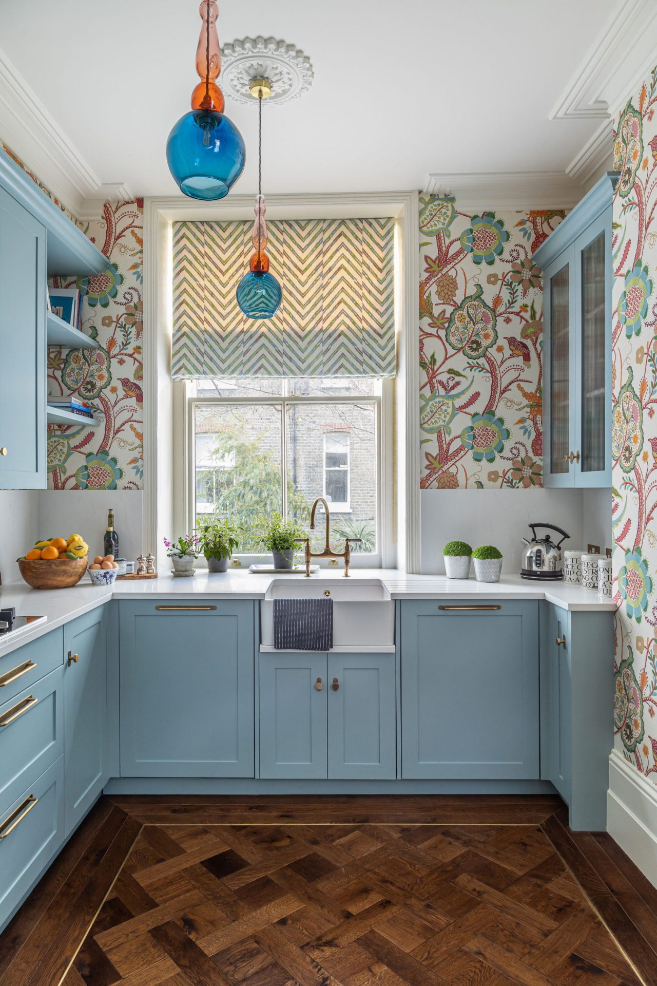 Kitchen with pale cabinetry, amber glass pendants and chevron parquet flooring