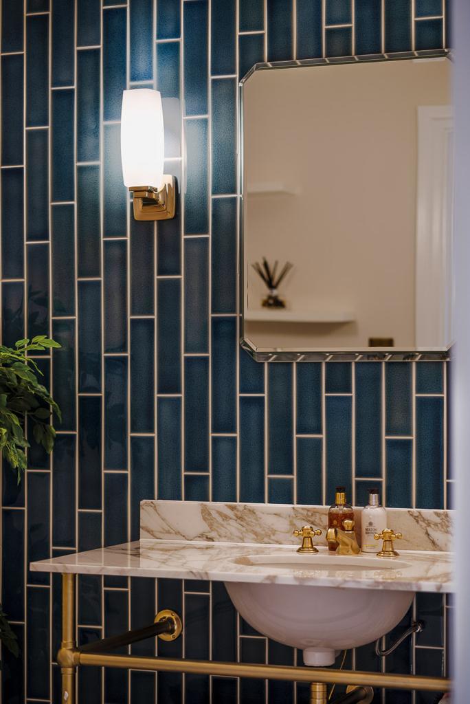 Powder room with teal subway tiles, marble counter and brass basin frame