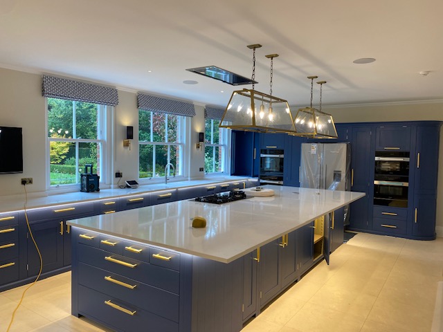 Kitchen with blue cabinetry, waterfall island and brass pendants